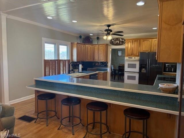 kitchen with light wood finished floors, black appliances, ornamental molding, and a sink