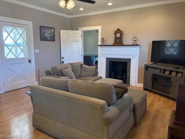 living room with ceiling fan, recessed lighting, a fireplace, light wood-type flooring, and crown molding