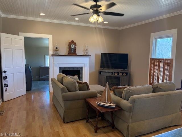 living room featuring light wood finished floors, crown molding, and a tiled fireplace