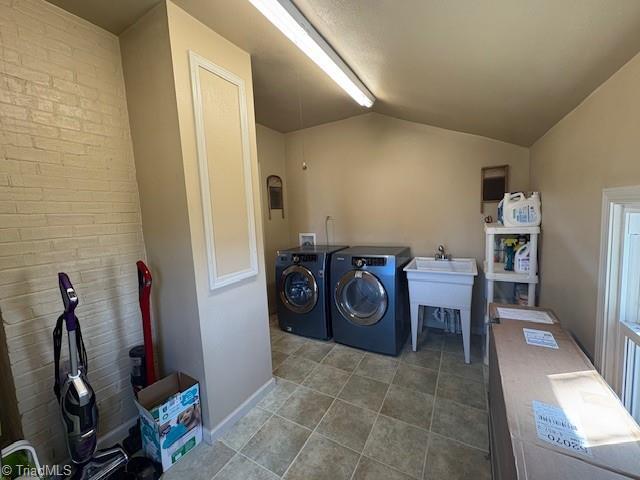 washroom featuring laundry area, washer and clothes dryer, tile patterned flooring, and brick wall