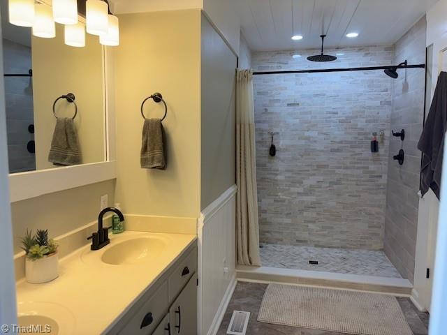 full bath featuring double vanity, visible vents, a sink, and tiled shower