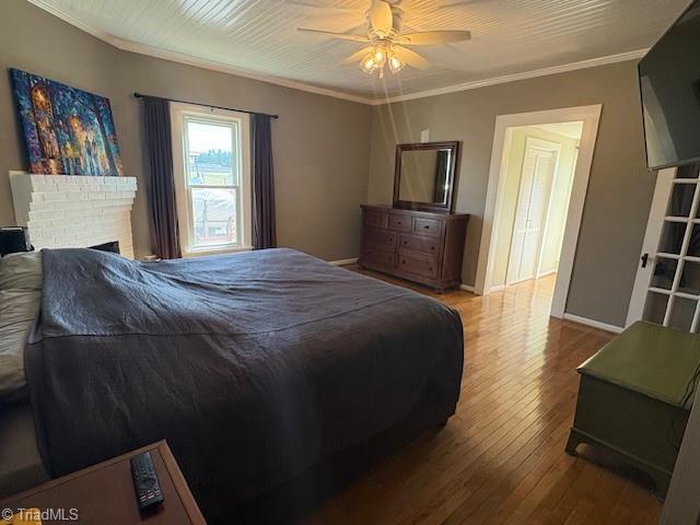 bedroom featuring a fireplace, wood-type flooring, ornamental molding, a ceiling fan, and baseboards