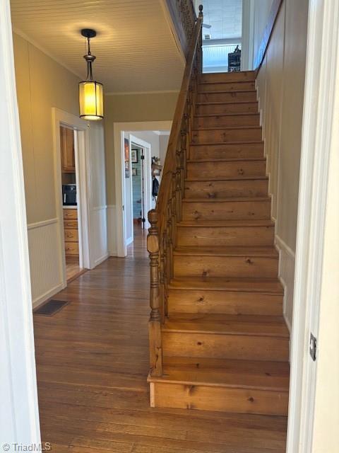 stairway with a wainscoted wall, visible vents, and wood finished floors