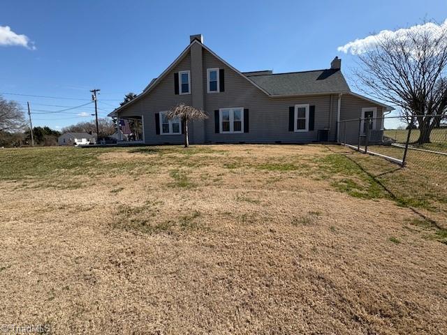 rear view of property with a lawn, a chimney, fence, and central air condition unit