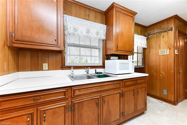kitchen featuring white microwave, a sink, brown cabinetry, and light countertops