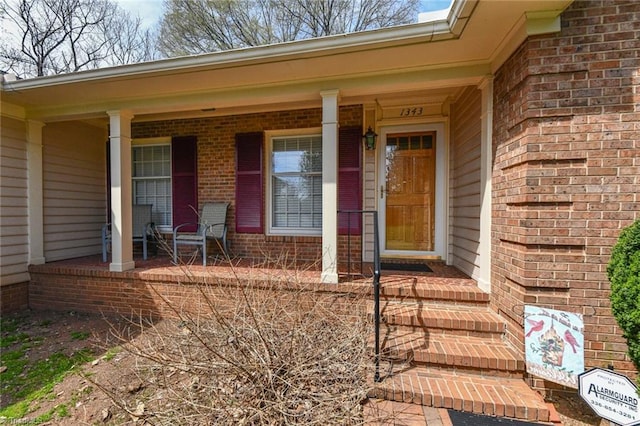 doorway to property featuring covered porch and brick siding