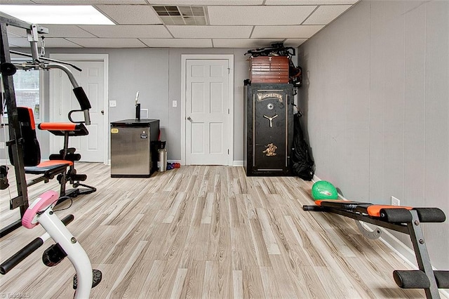 exercise room featuring light wood-type flooring and a paneled ceiling