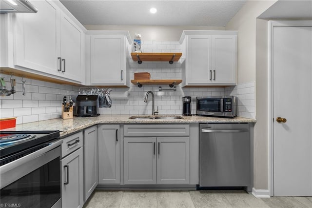 kitchen featuring stainless steel appliances, gray cabinets, decorative backsplash, a sink, and a textured ceiling