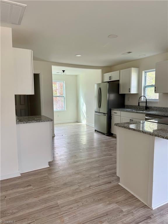 kitchen with white cabinets, light wood-type flooring, and stainless steel refrigerator