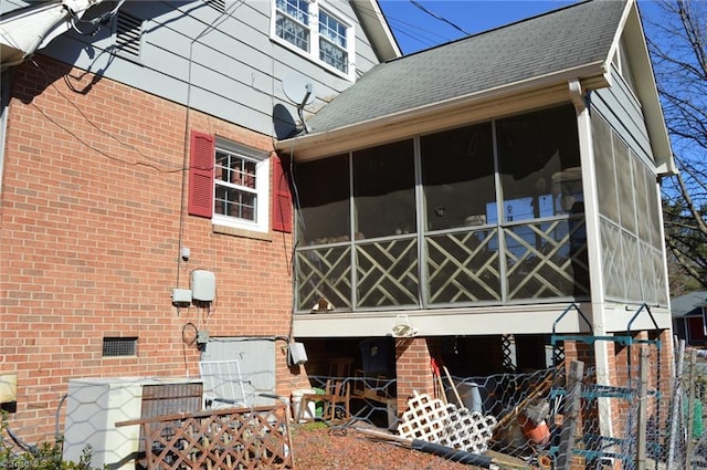 view of side of home featuring crawl space, a sunroom, brick siding, and roof with shingles