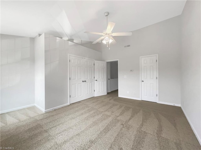 unfurnished bedroom featuring multiple closets, carpet floors, high vaulted ceiling, and ceiling fan