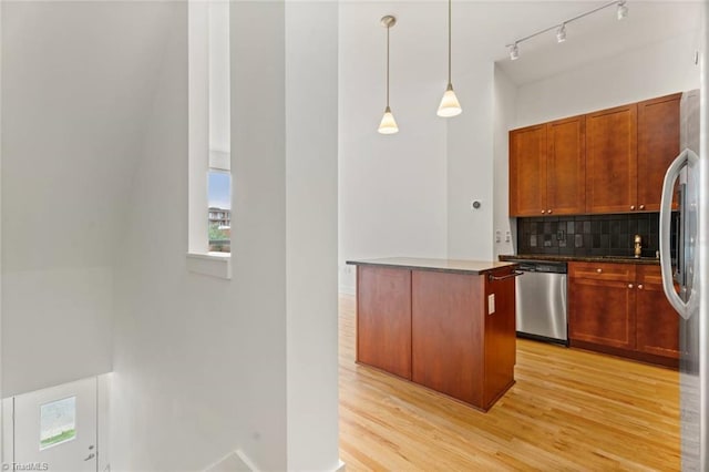 kitchen featuring appliances with stainless steel finishes, tasteful backsplash, light wood-type flooring, pendant lighting, and dark countertops