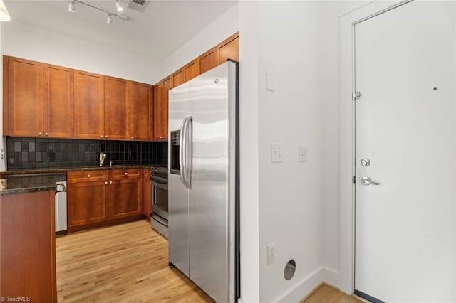 kitchen with stainless steel appliances, backsplash, light wood-style floors, dark stone countertops, and brown cabinetry