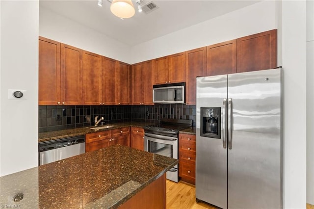 kitchen featuring appliances with stainless steel finishes, a sink, backsplash, dark stone countertops, and light wood-style floors