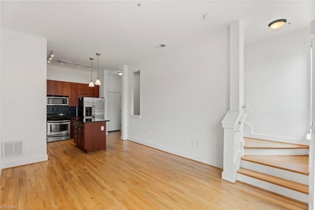 kitchen with stainless steel appliances, backsplash, open floor plan, and light wood finished floors