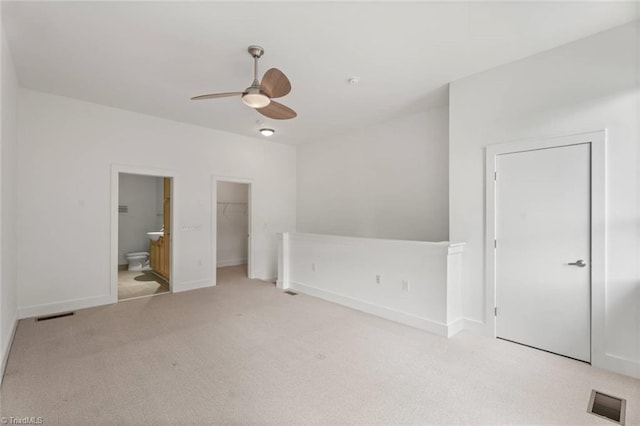 unfurnished bedroom featuring carpet, a spacious closet, ensuite bathroom, baseboards, and a ceiling fan