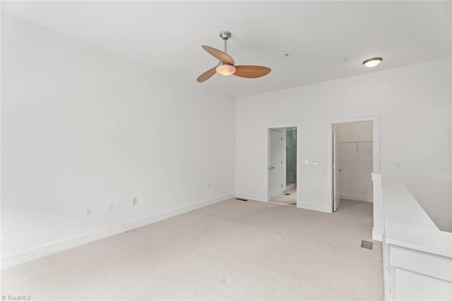 unfurnished bedroom with light colored carpet, a walk in closet, baseboards, a ceiling fan, and a closet