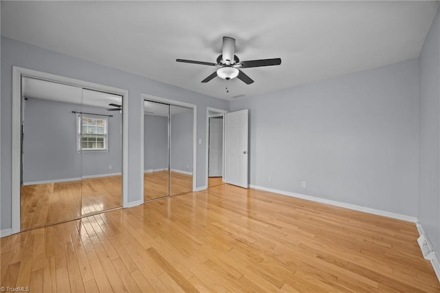 unfurnished bedroom with two closets, baseboards, light wood-style floors, and a ceiling fan