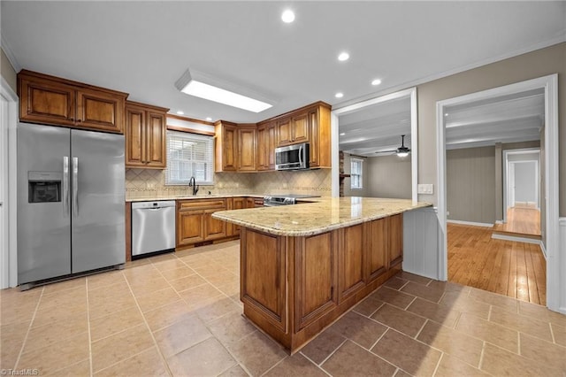 kitchen featuring brown cabinets, ornamental molding, tasteful backsplash, stainless steel appliances, and a peninsula