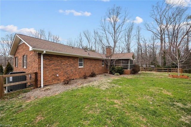 rear view of house featuring fence, a sunroom, a chimney, a lawn, and brick siding