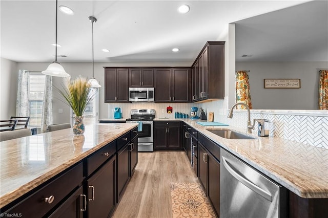 kitchen featuring stainless steel appliances, light wood-style floors, a sink, and light stone countertops