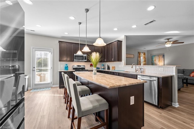 kitchen with dark brown cabinetry, a peninsula, visible vents, appliances with stainless steel finishes, and light wood finished floors