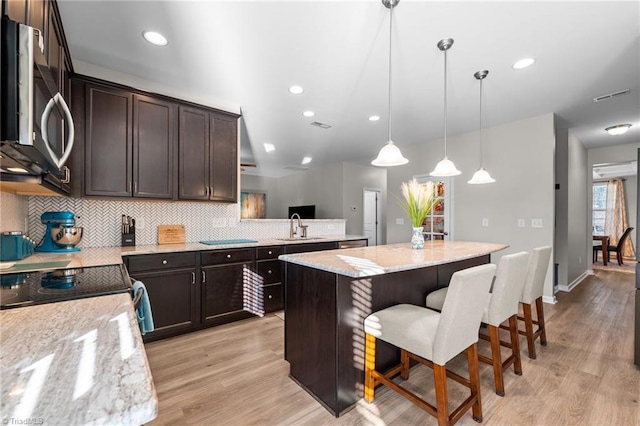 kitchen with light wood-style floors, stainless steel microwave, backsplash, and dark brown cabinets