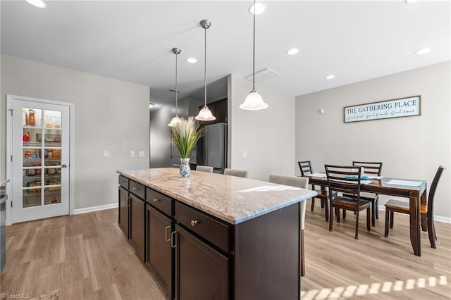 kitchen with light wood-type flooring, pendant lighting, dark brown cabinets, and refrigerator