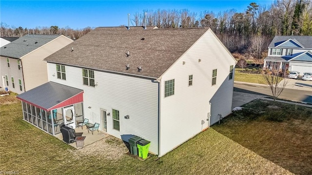 rear view of house with a sunroom, roof with shingles, a patio area, and a yard