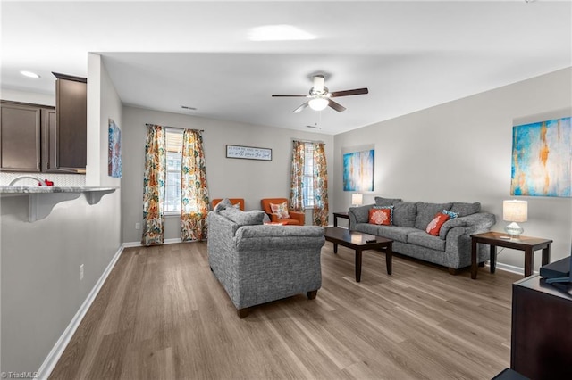 living area featuring baseboards, ceiling fan, and light wood finished floors