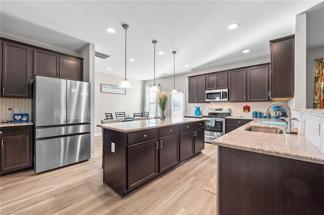 kitchen with stainless steel appliances, a sink, dark brown cabinets, a center island, and light wood finished floors