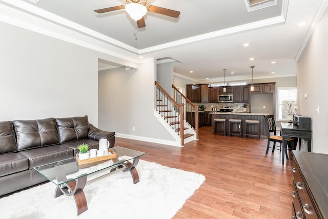 living room with ceiling fan, a tray ceiling, ornamental molding, and light hardwood / wood-style floors