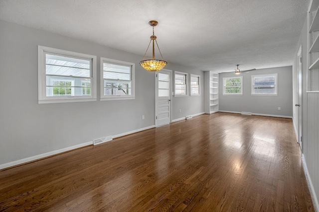 empty room with built in shelves, a textured ceiling, ceiling fan, and dark wood-type flooring