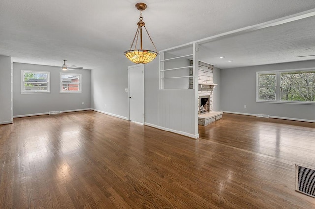 unfurnished living room with built in features, a stone fireplace, and dark wood-type flooring