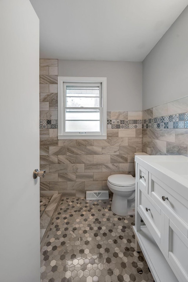 bathroom with tile walls, toilet, vanity, and tile floors