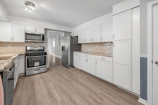 kitchen with white cabinets, appliances with stainless steel finishes, light stone countertops, tasteful backsplash, and light wood-type flooring