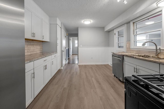 kitchen with appliances with stainless steel finishes, sink, light hardwood / wood-style flooring, white cabinets, and a textured ceiling