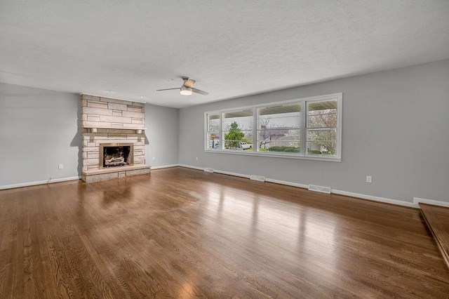 unfurnished living room featuring ceiling fan, a textured ceiling, a stone fireplace, and dark wood-type flooring