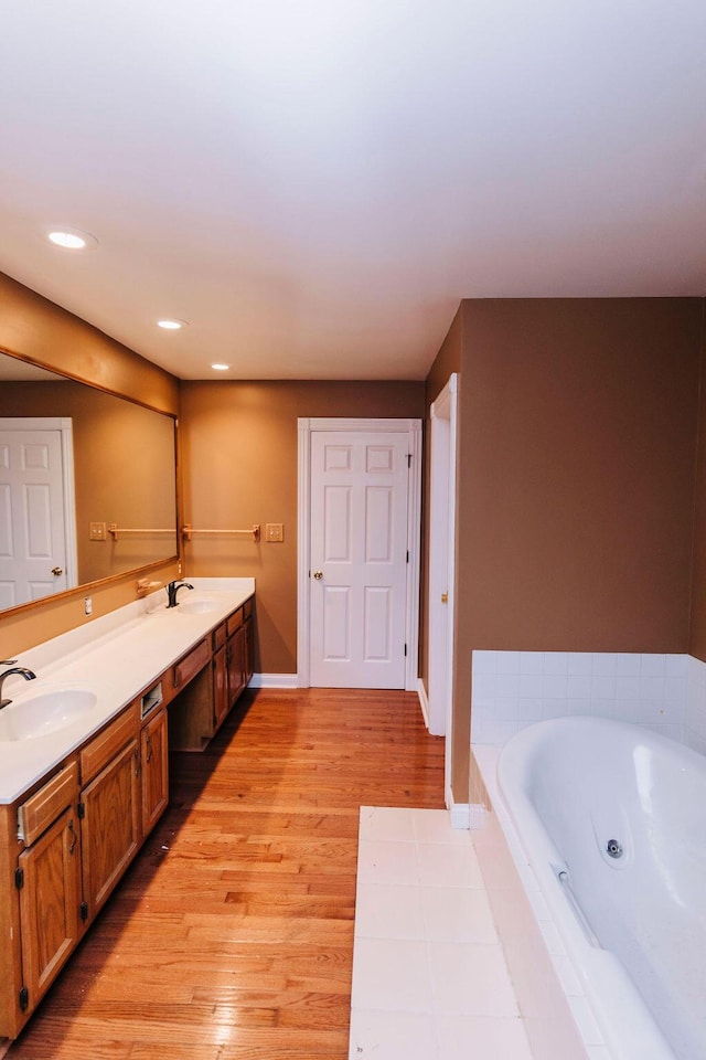 bathroom with dual vanity, hardwood / wood-style floors, and tiled tub