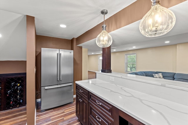 kitchen featuring stainless steel built in refrigerator, dark brown cabinetry, wood-type flooring, light stone counters, and pendant lighting