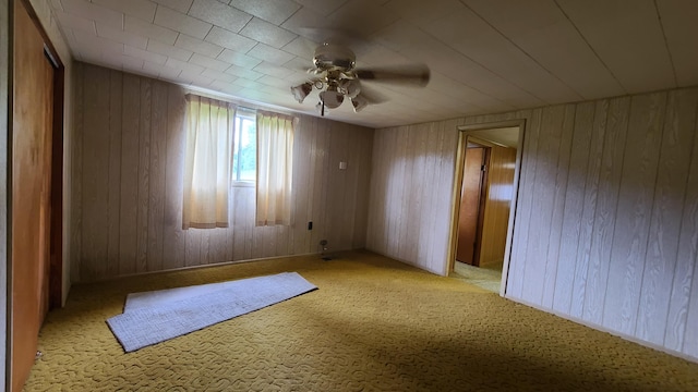 spare room with ceiling fan, wooden walls, and light colored carpet