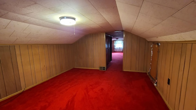 bonus room with wooden walls, vaulted ceiling, and dark carpet