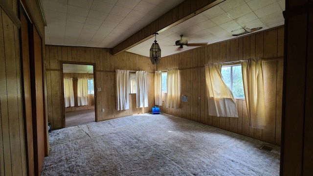 carpeted empty room with beam ceiling, wooden walls, and ceiling fan