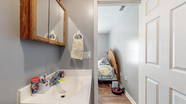 bathroom with a textured ceiling, wood-type flooring, and vanity with extensive cabinet space