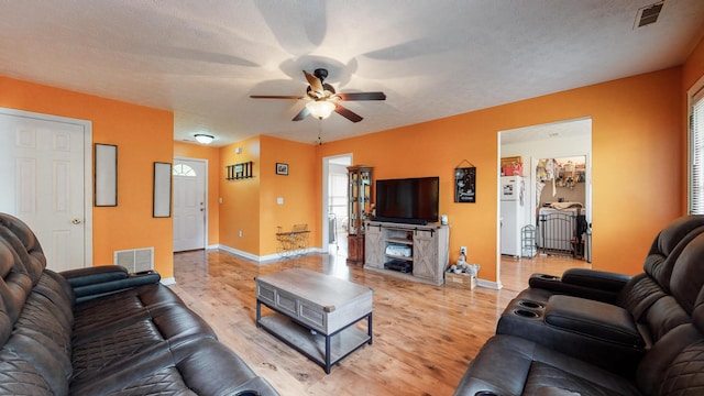 living room with a textured ceiling, ceiling fan, and light wood-type flooring