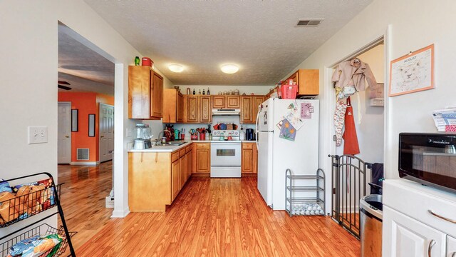 kitchen featuring white appliances, a textured ceiling, and light wood-type flooring