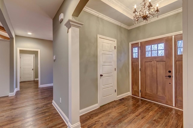 foyer with crown molding, an inviting chandelier, dark wood-type flooring, and ornate columns