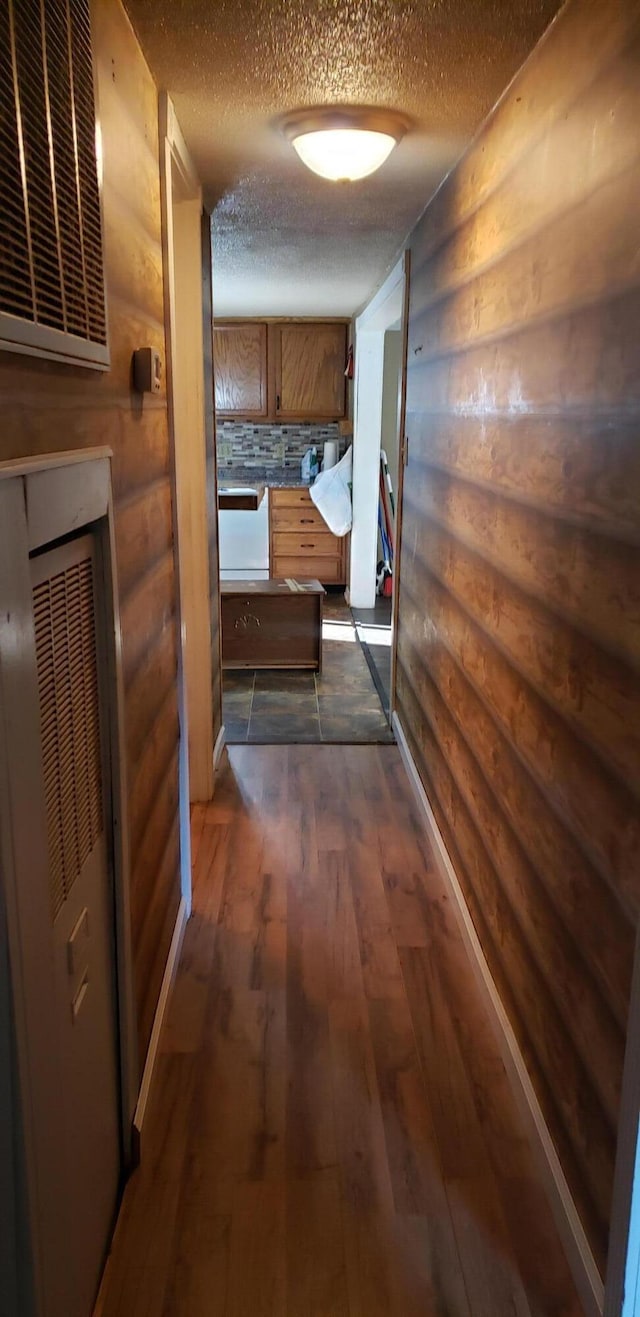 hall featuring wood walls, dark wood-type flooring, and a textured ceiling