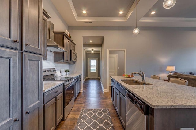 kitchen featuring appliances with stainless steel finishes, dark wood-type flooring, wall chimney range hood, decorative light fixtures, and sink