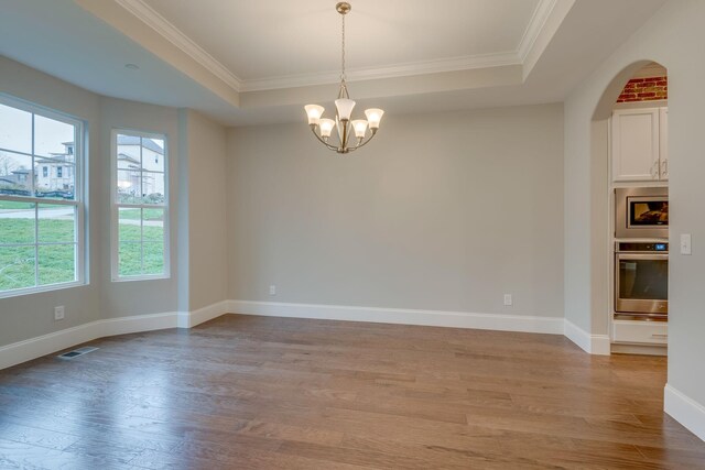 unfurnished room with a notable chandelier, crown molding, a tray ceiling, and light hardwood / wood-style floors